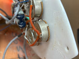 Close-up of a white plastic electronic control module with two silver rotary potentiometers, orange wire, and attached wires on a workshop surface.