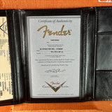 Fender certificate of authenticity in a black leather case on an orange surface