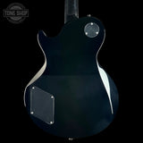 The rear view of a black electric guitar with a glossy finish, featuring a chrome-silver circular control and a black plate, set against a solid black background.