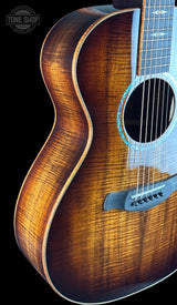 Close-up of an acoustic guitar body showing a rich brown flamed wood finish, sound hole, bridge, and part of the neck against a black background.