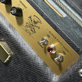 Close-up of a guitar control panel with a brushed gold metal plate, black textured fabric body, silver toggle switches labeled POWER and STANDBY, and a red illuminated indicator light. The plate includes printed graphics and the text 'SUPER FIFTY-NINE' and 'PRESENCE'.