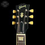 Close-up of a Gibson electric guitar headstock with six yellow tuning pegs, gold lettering, and a black finish against a black background.