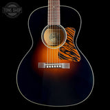 A close-up studio shot of an acoustic guitar body against a black background, showing a dark blue to brown sunburst finish, white binding, a tiger-stripe style pickguard, and a silver bridge. A Tone Shop watermark is visible in the top left corner.