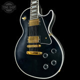 Black electric guitar with gold hardware on a black background, featuring 'Tone Shop' logo.