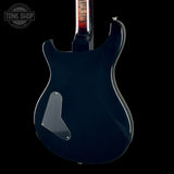 The rear view of an electric guitar with a glossy dark navy blue body, a silver pickguard, and a black headstock, shown against a solid black background with a Tone Shop watermark in the top left corner.