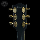 Close-up of a guitar headstock with gold tuning pegs on a black background, featuring the 'Tone Shop' logo.