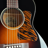 Close-up of an acoustic guitar body showing the orange and black tiger-stripe pickguard, sunburst wood finish, sound hole, and part of the neck against a black background.