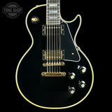 Black electric guitar with gold hardware on a black background, featuring 'Tone Shop' logo.