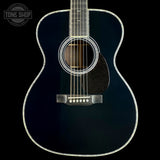 A close-up studio shot of an acoustic guitar body against a black background, showing a glossy dark blue finish, white rosette, pickguard, and binding, with six strings visible. A Tone Shop logo watermark is in the top-left corner.