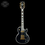 Electric guitar with black finish and gold hardware on a black background, featuring 'Tone Shop' logo.