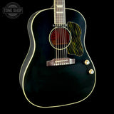 A close-up of a dark acoustic-electric guitar body with gold-toned hardware, a black pickguard with wood grain, and a white binding edge, shown against a black background with a Tone Shop watermark in the upper left.