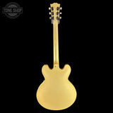 A gold-finish double-cutaway electric guitar shown from the back against a solid black background, with a Tone Shop watermark in the top-left corner.