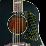 Close-up of a Gibson acoustic guitar body showing the round soundhole, six strings, part of the fretboard, and a decorative green-and-gold striped pickguard against a black background.
