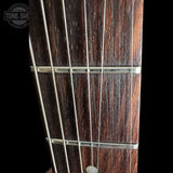 Close-up of a guitar fretboard made of dark brown wood with silver metal frets and strings, shown against a black background with a Tone Shop watermark in the top left corner.