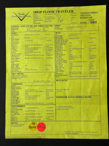 A yellow Shop Floor Traveler work order form with printed tables, signatures, and a red circular stamp, photographed flat against a dark background.