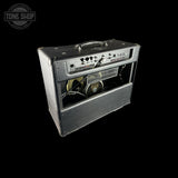 A vintage black guitar amplifier with a silver control panel and visible speaker inside, shown on a solid black background. A Tone Shop watermark is visible in the top-left corner.