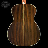 Close-up of the back of an acoustic guitar showing a rich dark brown wood grain finish with a light cream binding, set against a solid black background.