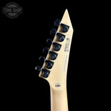 Close-up of the headstock of an electric guitar against a solid black background, showing six black tuning pegs, a light natural wood neck, and a white backplate with printed specifications.