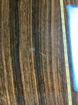 Close-up of a dark brown wood grain surface with a small white scratch or mark near the center and a bright blue-white light reflection along the right edge.