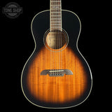 An acoustic guitar with a natural wood sunburst finish, shown from the front against a solid black background. A circular 'TONE SHOP' watermark is visible in the top-left corner.