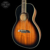 A close-up of a acoustic guitar against a solid black background, showing the sunburst wood finish, sound hole, bridge, and part of the neck. A circular 'TONE SHOP' watermark is visible in the top-left corner.