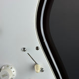 Close-up detail of an electric guitar's control panel, showing a white volume/tone knob, chrome screws, a silver tremolo arm, and a glossy black pickguard.