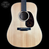 A natural wood acoustic guitar shown from the front against a solid black background, featuring a flamed maple top, dark pickguard, and black bridge. A Tone Shop watermark is visible in the top-left corner.