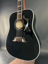 Black acoustic guitar with decorative inlay on a dark surface