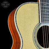 Close-up of an acoustic guitar body showing the natural wood grain side, the light beige backplate, and part of the dark fretboard against a black background. A 'TONE SHOP' watermark is visible in the top-left corner.