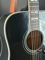 Close-up of a black acoustic guitar with a visible brand logo on the soundhole.