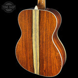 Close-up of the back of an acoustic guitar showing rich wood grain patterns in warm brown tones with a light natural wood center stripe, set against a solid black background.