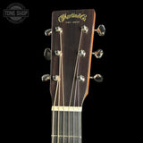 Close-up of the headstock of a Martin & Co acoustic guitar against a black background, showing the brand name in gold script and six tuning pegs.