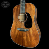 A close-up of an acoustic guitar body showing a rich, warm brown wood grain finish, a black pickguard, and a silver bridge, set against a solid black background with a Tone Shop watermark in the top-left corner.