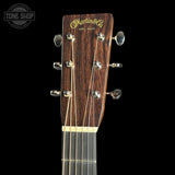 Martin & Co acoustic guitar headstock in dark brown wood with gold lettering, six silver tuning pegs, and four strings, shown against a solid black background.