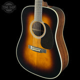 A classic acoustic guitar with a natural sunburst finish, showing a dark brown center fading to a warm amber-orange edge, photographed against a solid black background.