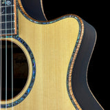 Close-up of a Taylor acoustic guitar body showing the natural wood grain, sound hole rosette, and dark side edge against a black background.