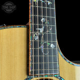 Close-up of a natural wood acoustic guitar body and neck with iridescent mother-of-pearl floral inlays on the fretboard, set against a black background. A Tone Shop watermark is visible in the top-left corner.