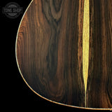 Close-up of a guitar body showing dark brown wood grain with a light tan inlay stripe down the center, photographed against a black background. A Tone Shop watermark is visible in the upper left corner.