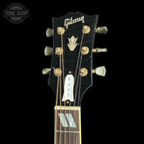 Close-up of a Gibson acoustic guitar headstock in black, showing gold tuning pegs, a white Dove logo plaque, and the Gibson brand name on a black background.