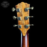 Close-up of a guitar headstock with six metallic tuning pegs and circular black-and-gold Tunemaster logos, set against a solid black background. A Tone Shop watermark is visible in the top-left corner.