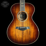 A close-up studio shot of the front of an acoustic guitar against a black background, showing a bright natural wood finish with prominent grain, a black soundhole surround, and a Tone Shop logo overlay in the top left corner.