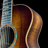 Close-up of an acoustic guitar body showing a rich, warm brown wood grain finish, the sound hole with a blue inlay, and part of the dark fretboard against a black background.
