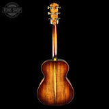 The back of an acoustic guitar with a glossy sunburst finish showing vibrant brown wood grain, photographed against a solid black background with a Tone Shop watermark in the top left corner.