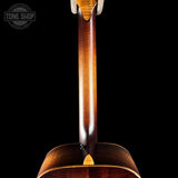 Close-up of the neck and upper body of a wooden acoustic guitar against a solid black background, with a Tone Shop watermark in the top-left corner.