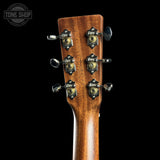 Close-up of the headstock of a wooden acoustic guitar, showing six tuning pegs and decorative metal tuning caps on a black background. A Tone Shop watermark is visible in the top left corner.