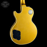 The back of a gold-finish electric guitar, likely a Gibson Les Paul Custom, shown against a solid black background. Features a circular 'Gibson Les Paul Custom' badge on the upper back and a black pickguard.