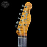 Close-up of a Fender Telecaster electric guitar headstock with a natural wood finish, six silver tuning pegs, and the Fender logo, shown against a black background.