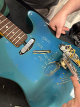 Blue electric guitar with visible wiring and a person's hand adjusting components.