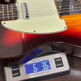 A close-up of a guitar body resting on a digital scale, showing the scale reading 6.36 oz.