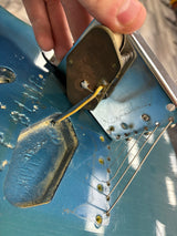 Close-up of a guitar's bridge with a hand adjusting a string.